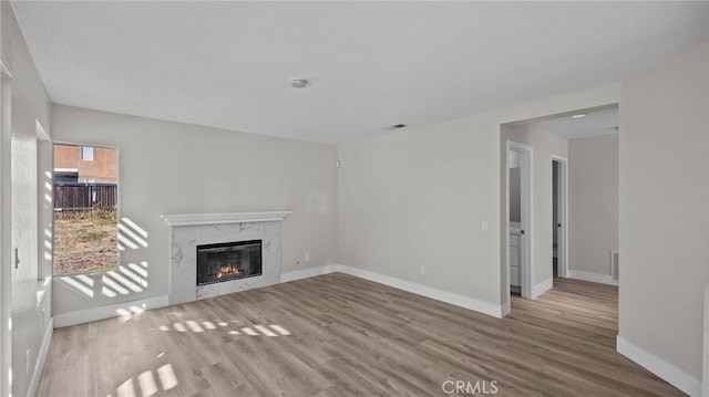 unfurnished living room with a premium fireplace, wood finished floors, visible vents, and baseboards