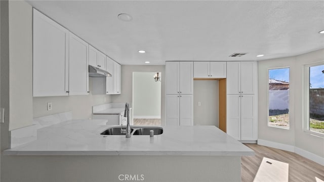 kitchen featuring a peninsula, light stone counters, a sink, and under cabinet range hood