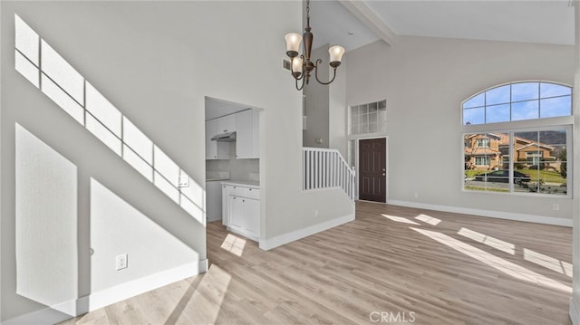 unfurnished living room with an inviting chandelier, high vaulted ceiling, beamed ceiling, and light wood-type flooring