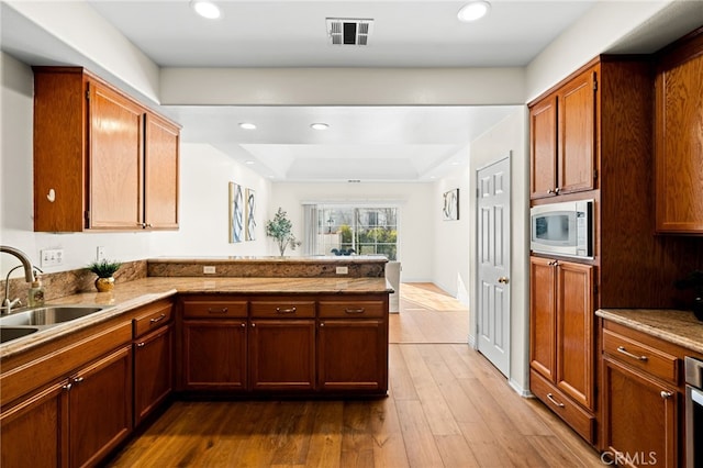 kitchen featuring sink, stainless steel microwave, a tray ceiling, light hardwood / wood-style floors, and kitchen peninsula