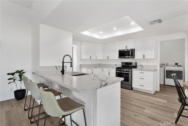 kitchen with kitchen peninsula, appliances with stainless steel finishes, white cabinets, a tray ceiling, and washing machine and clothes dryer