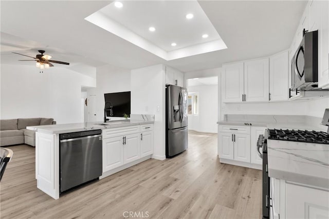 kitchen with kitchen peninsula, sink, white cabinetry, a tray ceiling, and stainless steel appliances