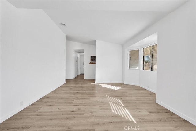 spare room featuring light wood-type flooring and vaulted ceiling