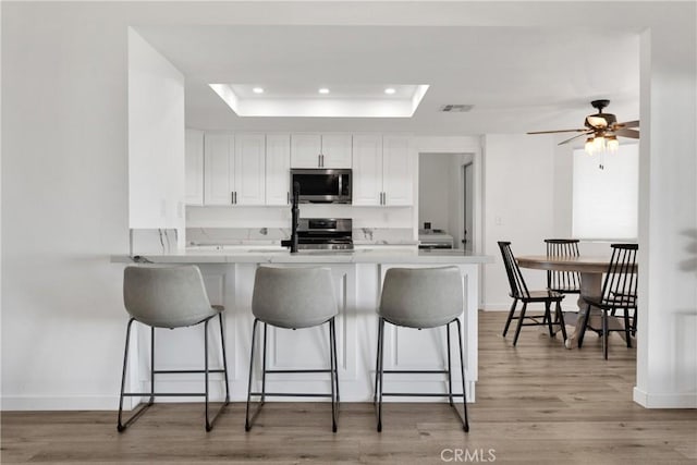 kitchen featuring appliances with stainless steel finishes, white cabinetry, a kitchen breakfast bar, kitchen peninsula, and a raised ceiling