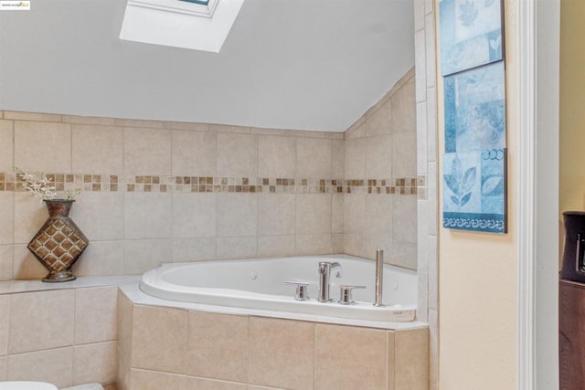 bathroom with vaulted ceiling with skylight and tiled tub