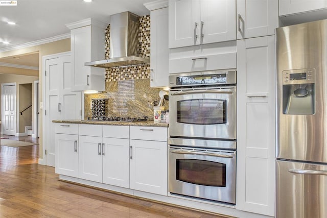 kitchen featuring tasteful backsplash, white cabinets, stainless steel appliances, light stone counters, and wall chimney exhaust hood