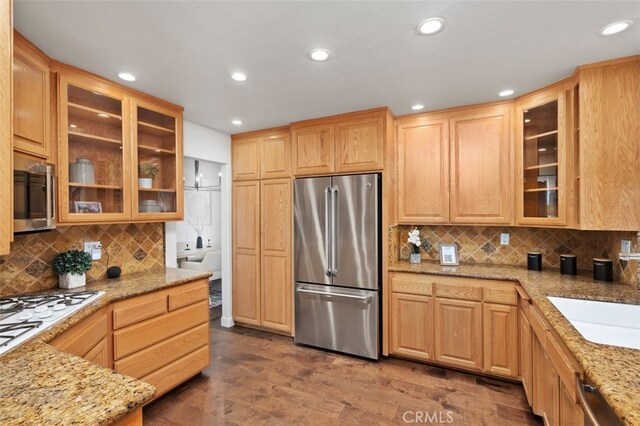 kitchen with light stone counters, backsplash, stainless steel appliances, and hardwood / wood-style floors