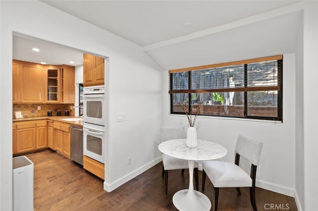 kitchen with white double oven, backsplash, glass insert cabinets, wood finished floors, and baseboards