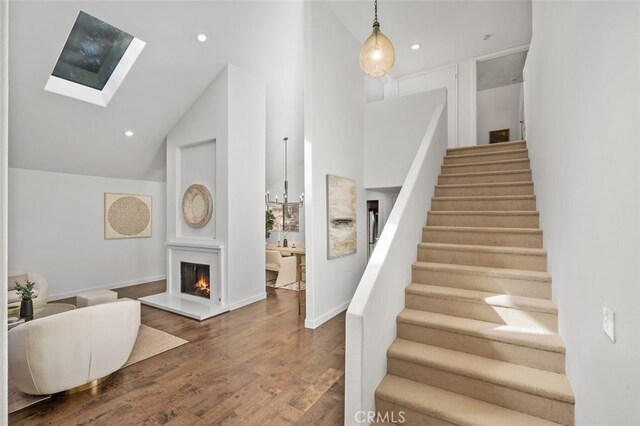 staircase featuring hardwood / wood-style floors, a skylight, and high vaulted ceiling