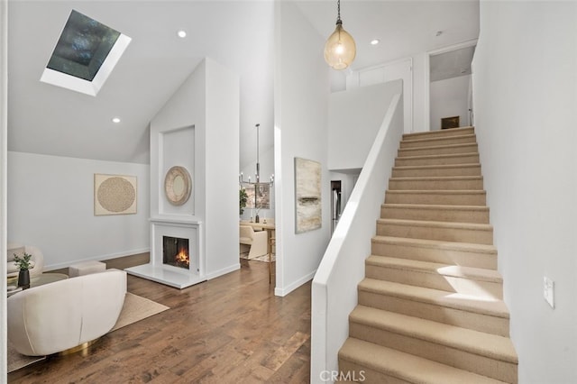 entryway featuring a warm lit fireplace, a skylight, stairway, wood finished floors, and recessed lighting