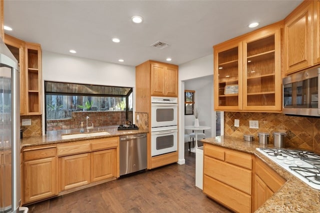 kitchen featuring light stone countertops, dark wood-type flooring, stainless steel appliances, and a sink