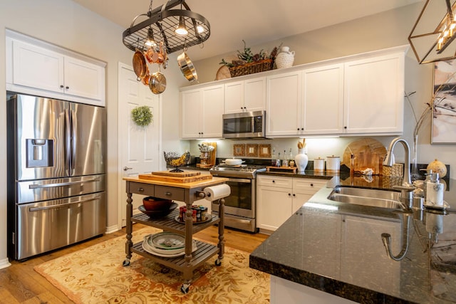 kitchen with sink, white cabinetry, pendant lighting, stainless steel appliances, and light hardwood / wood-style floors