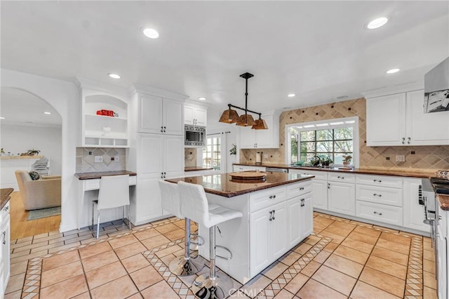 kitchen with a center island, light tile patterned floors, white cabinets, stainless steel microwave, and pendant lighting