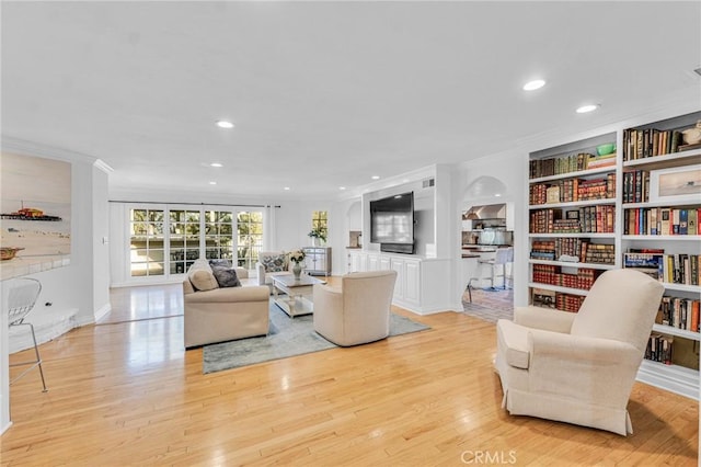 living room with ornamental molding, built in shelves, and light hardwood / wood-style floors