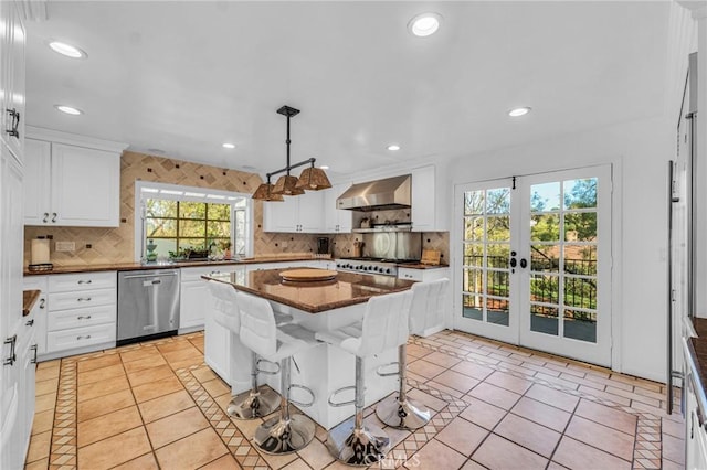 kitchen with a center island, decorative light fixtures, appliances with stainless steel finishes, wall chimney range hood, and a kitchen breakfast bar