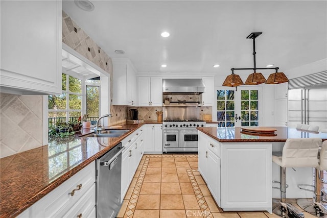 kitchen with decorative light fixtures, stainless steel appliances, white cabinetry, and wall chimney range hood