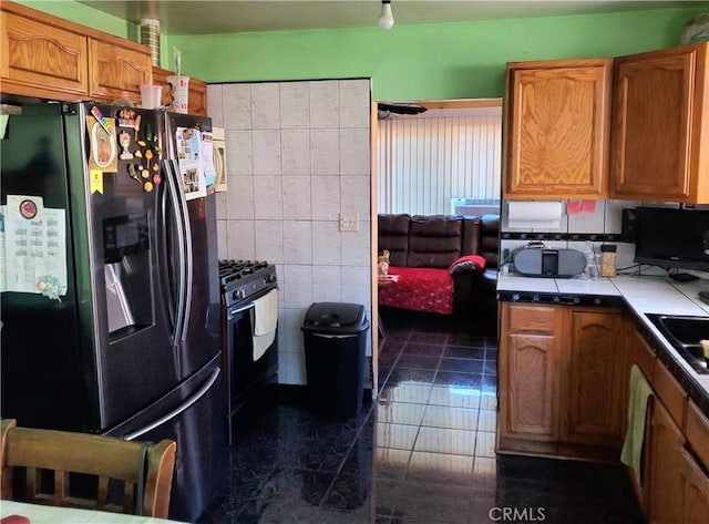 kitchen with tile walls, sink, range with gas cooktop, refrigerator with ice dispenser, and tile countertops