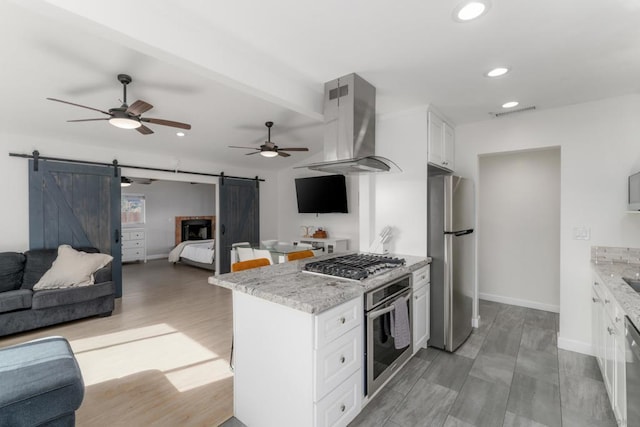 kitchen with light stone countertops, white cabinets, appliances with stainless steel finishes, island range hood, and a barn door