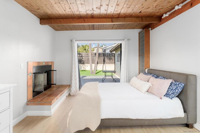 bedroom featuring wood ceiling, light wood-type flooring, beam ceiling, and a tile fireplace