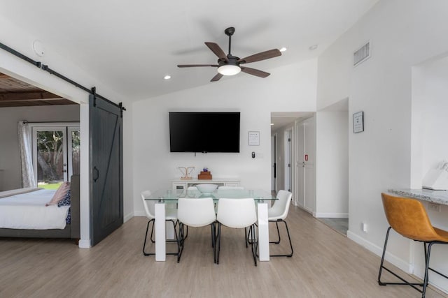 dining area featuring ceiling fan, light wood-type flooring, lofted ceiling, and a barn door