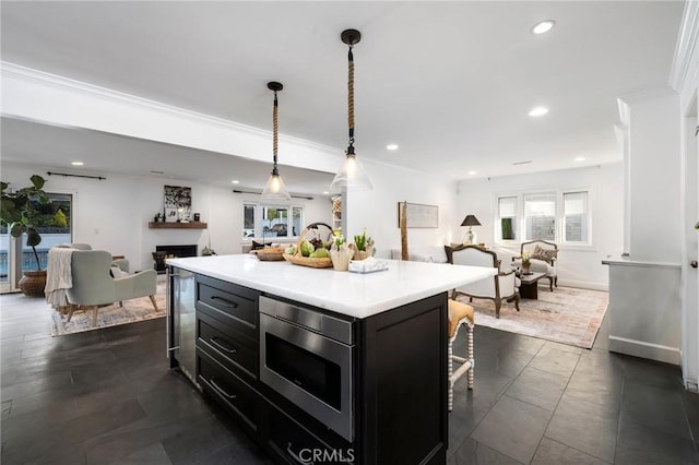 kitchen featuring a center island, stainless steel microwave, a kitchen bar, crown molding, and hanging light fixtures