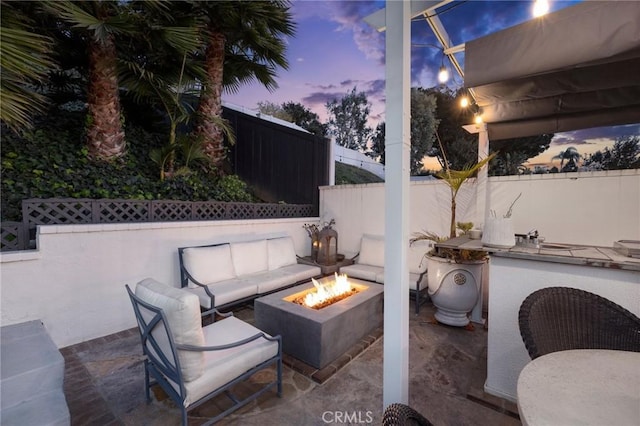 patio terrace at dusk featuring exterior kitchen and a fire pit