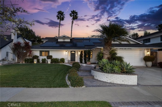 view of front of house with a garage, a yard, and solar panels