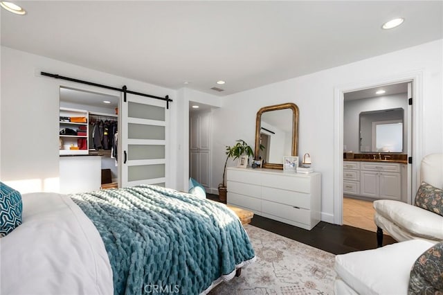 bedroom featuring a walk in closet, sink, a closet, ensuite bathroom, and a barn door