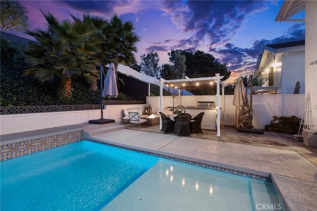 pool at dusk featuring a patio area and an outdoor kitchen