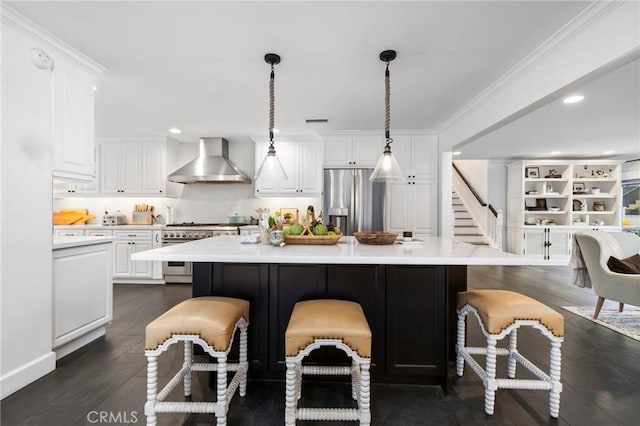 kitchen with appliances with stainless steel finishes, wall chimney exhaust hood, decorative light fixtures, white cabinets, and a kitchen bar