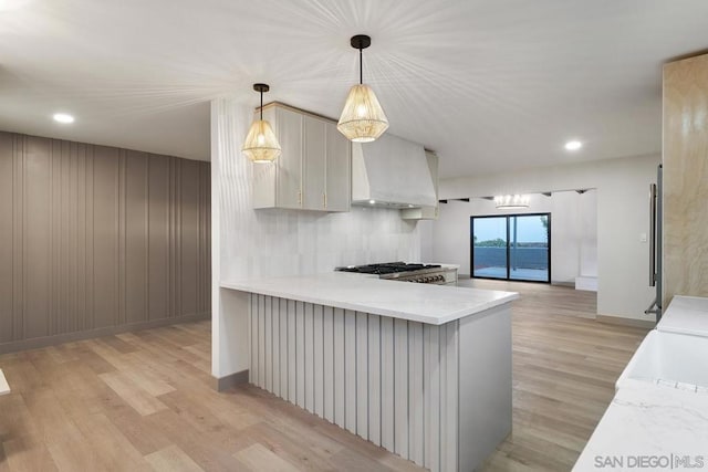 kitchen with pendant lighting, kitchen peninsula, stainless steel gas cooktop, light hardwood / wood-style flooring, and custom range hood