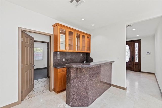 kitchen featuring kitchen peninsula, tasteful backsplash, and dark stone counters