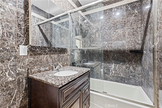 bathroom with combined bath / shower with glass door, vanity, and tile walls