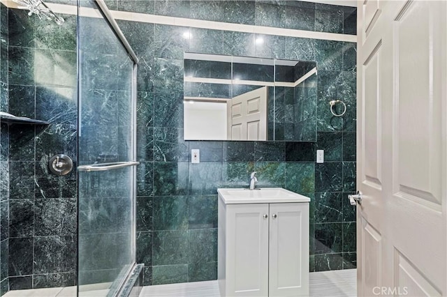 bathroom with a shower with door, vanity, and tile walls