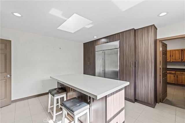 kitchen with a kitchen breakfast bar, stainless steel built in fridge, light tile patterned flooring, a center island, and a skylight