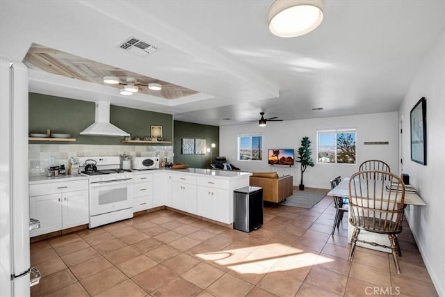 kitchen featuring white appliances, white cabinetry, kitchen peninsula, ceiling fan, and wall chimney exhaust hood