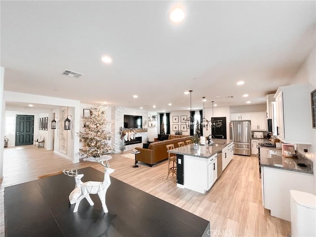 kitchen with white cabinets, stainless steel fridge, and an island with sink