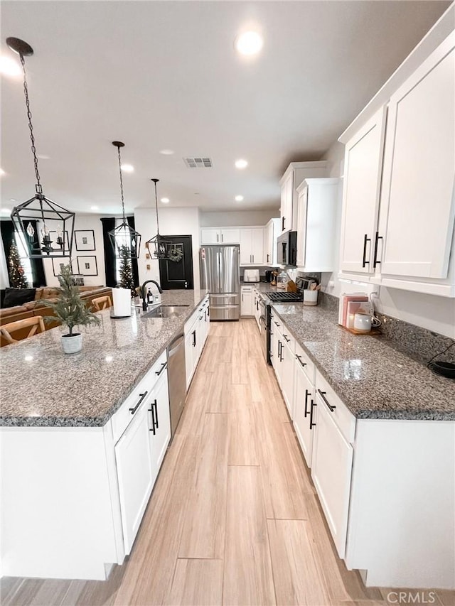 kitchen with a spacious island, appliances with stainless steel finishes, white cabinetry, sink, and hanging light fixtures