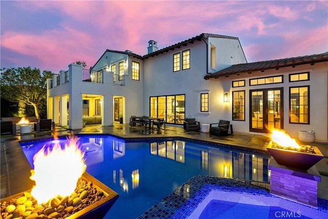 back house at dusk featuring a balcony, a patio, and a fire pit