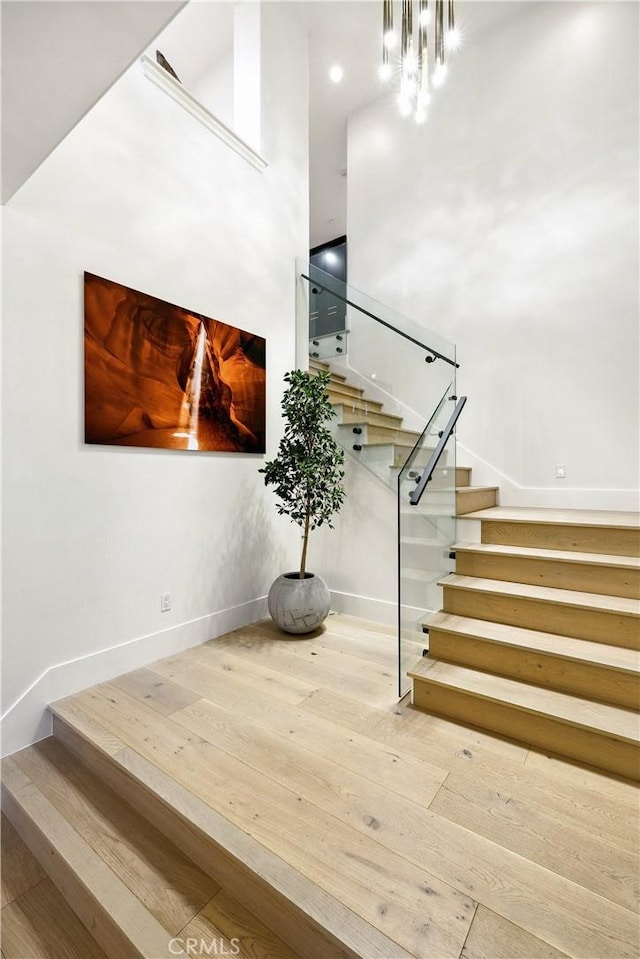 stairs with hardwood / wood-style flooring, a towering ceiling, and a notable chandelier