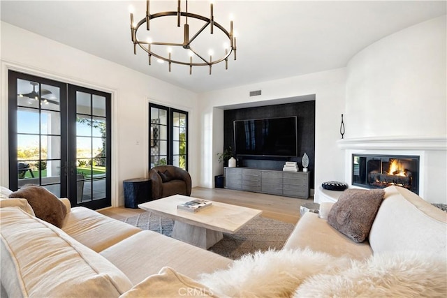 living room with french doors, a large fireplace, light hardwood / wood-style flooring, and a notable chandelier