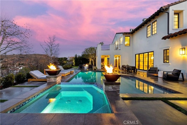 pool at dusk with an in ground hot tub, a patio area, and an outdoor fire pit