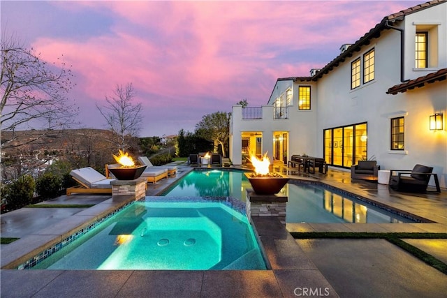 pool at dusk featuring an outdoor fire pit, a pool with connected hot tub, and a patio area