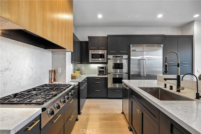 kitchen with sink, built in appliances, light stone counters, tasteful backsplash, and light hardwood / wood-style floors