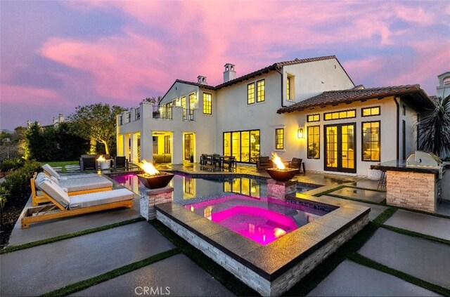 25551 Prado De Oro, Calabasas, CA 91302 - back of house at dusk with a fire pit, an outdoor kitchen, an in-ground hot tub, a balcony, and a patio area