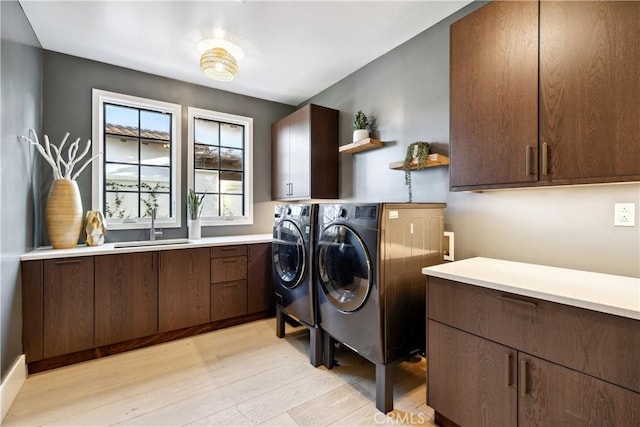 laundry area featuring sink, light hardwood / wood-style flooring, washing machine and dryer, and cabinets