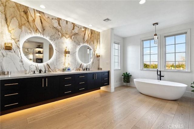 bathroom featuring double vanity, a soaking tub, wood-type flooring, a sink, and recessed lighting