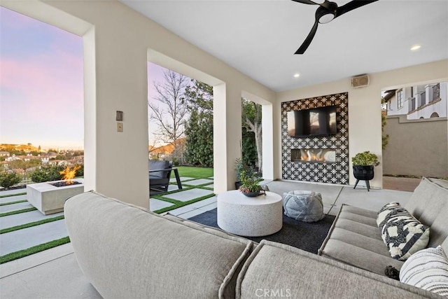 patio terrace at dusk featuring an outdoor living space with a fireplace and ceiling fan