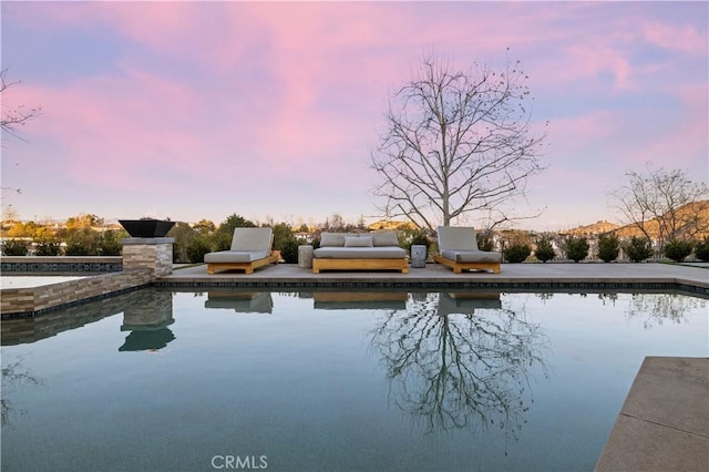 pool at dusk with an outdoor pool and a patio