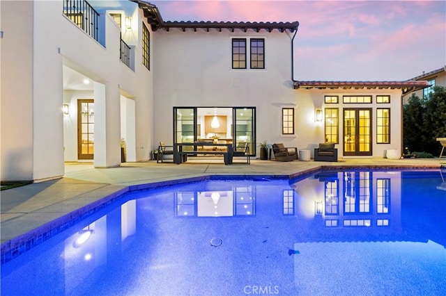 pool at dusk featuring a patio and french doors